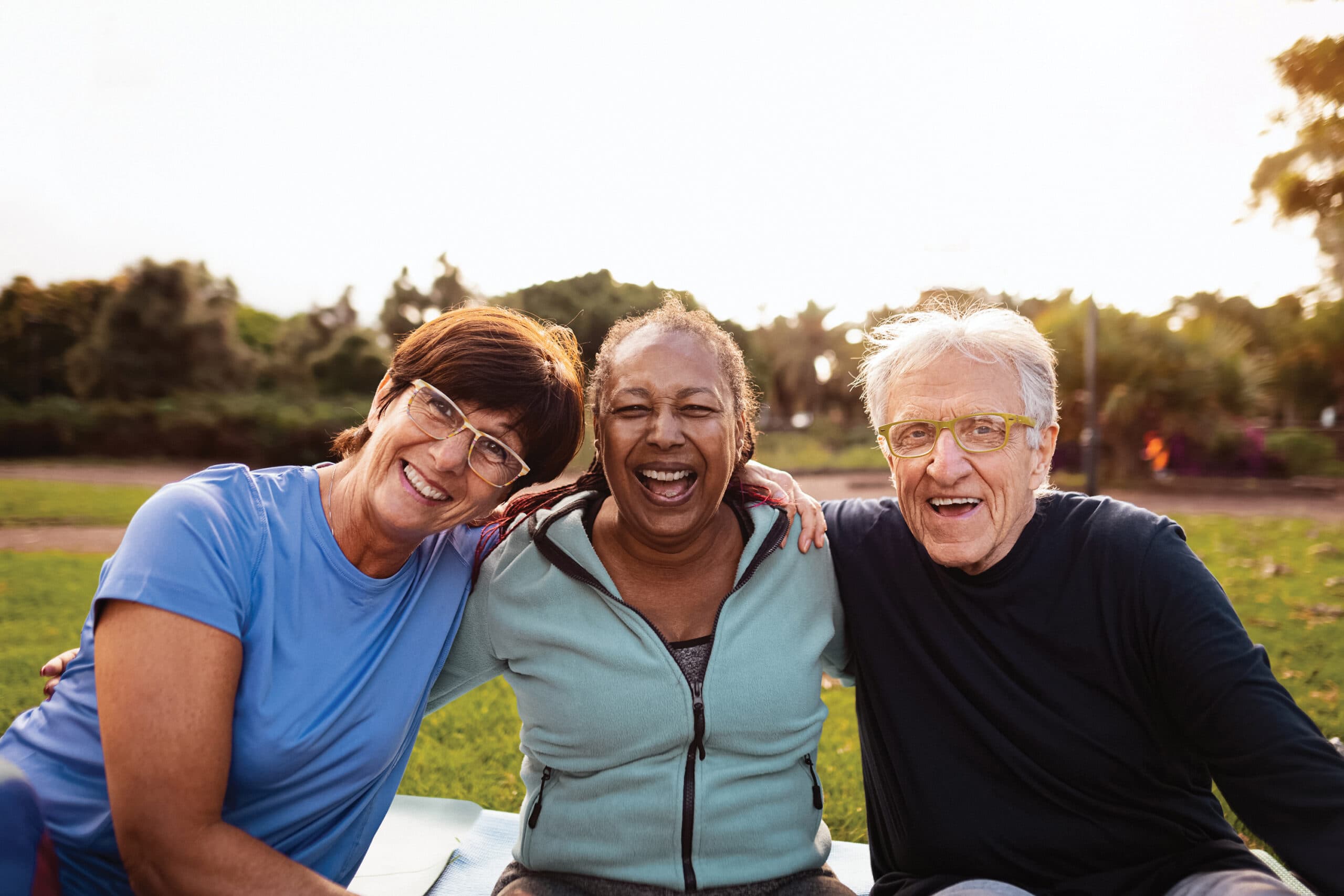 A group of three friends smiles for the camera while sitting outdoors.