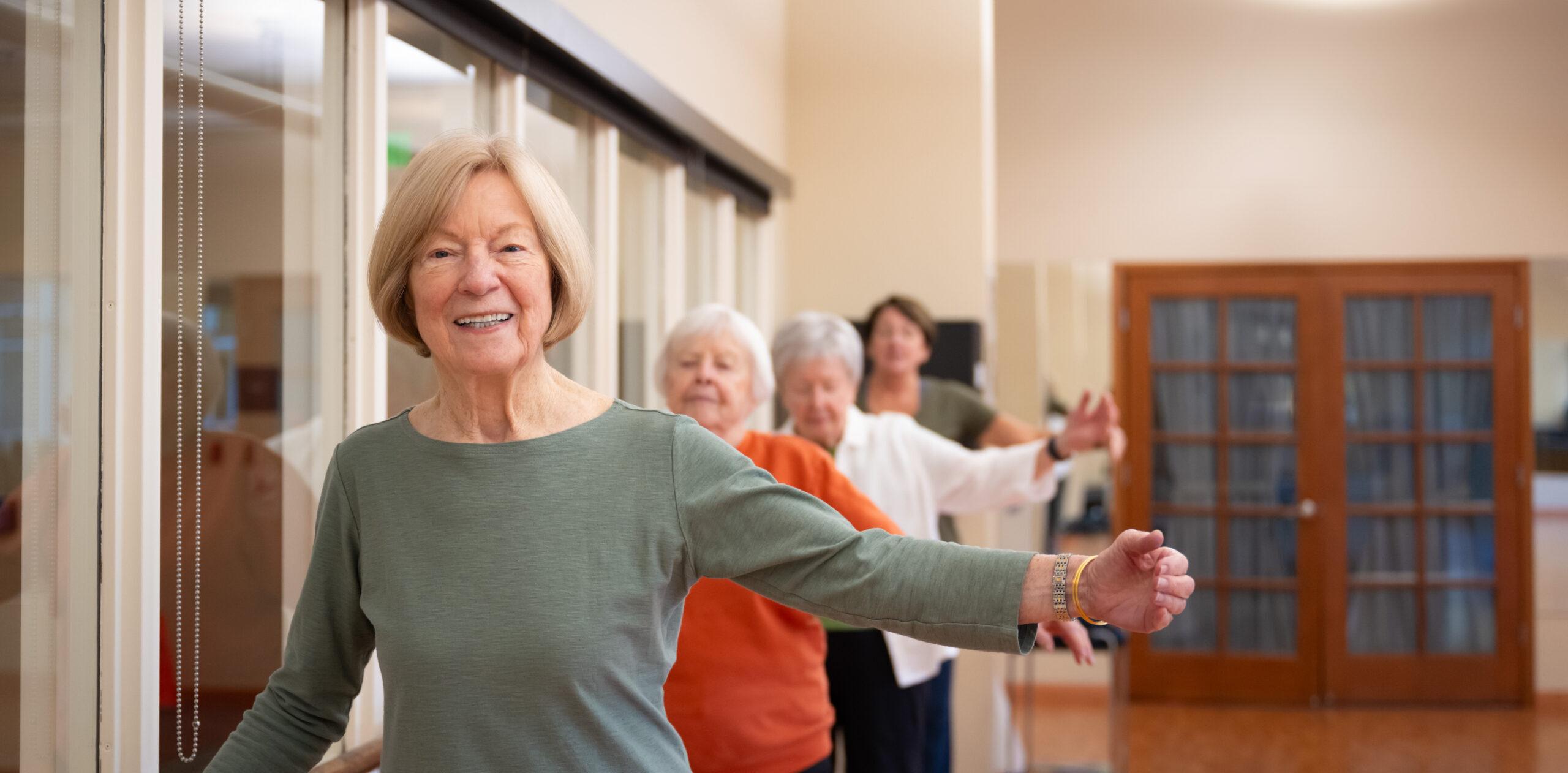 Several older adults practice a dance move while holding a hand rail.