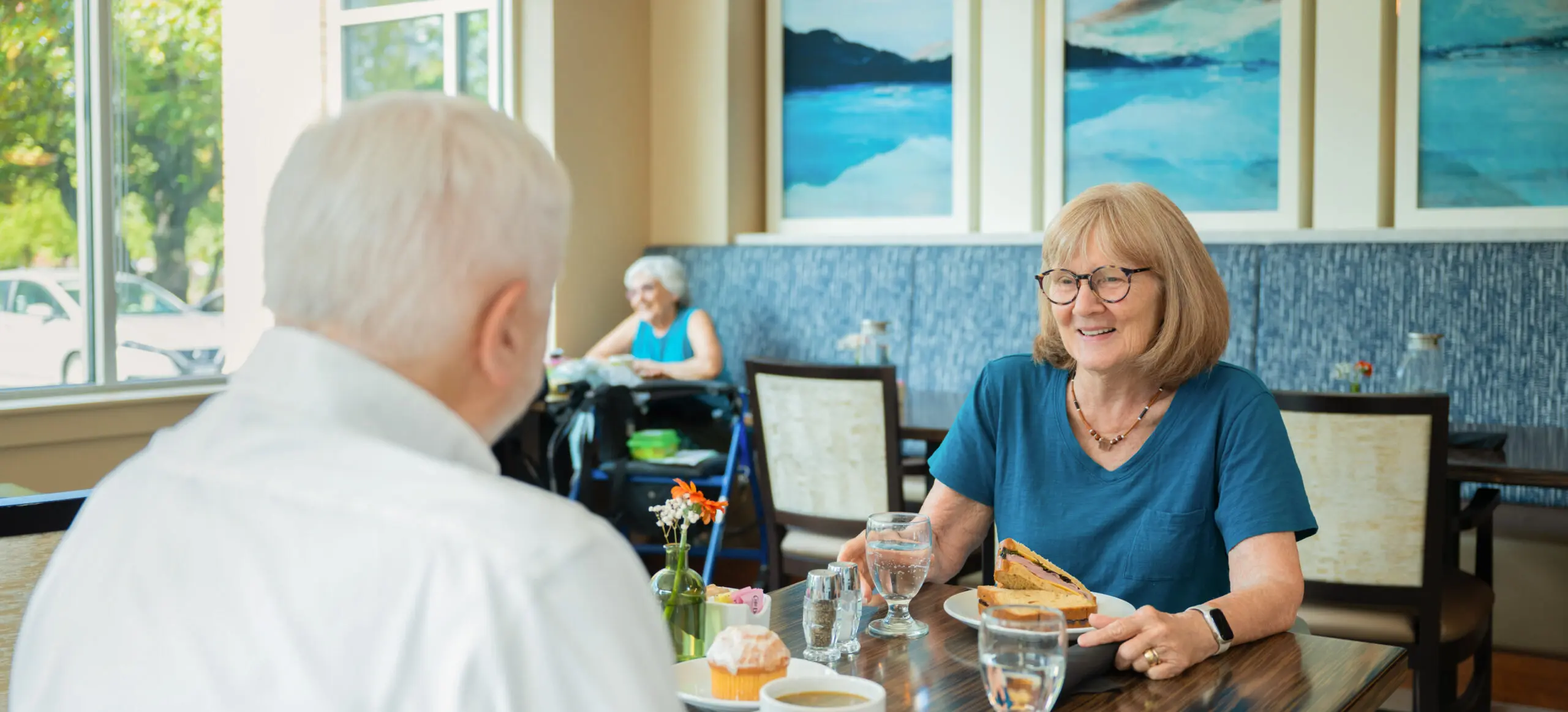An older woman smiles at someone sitting across the table over a meal.